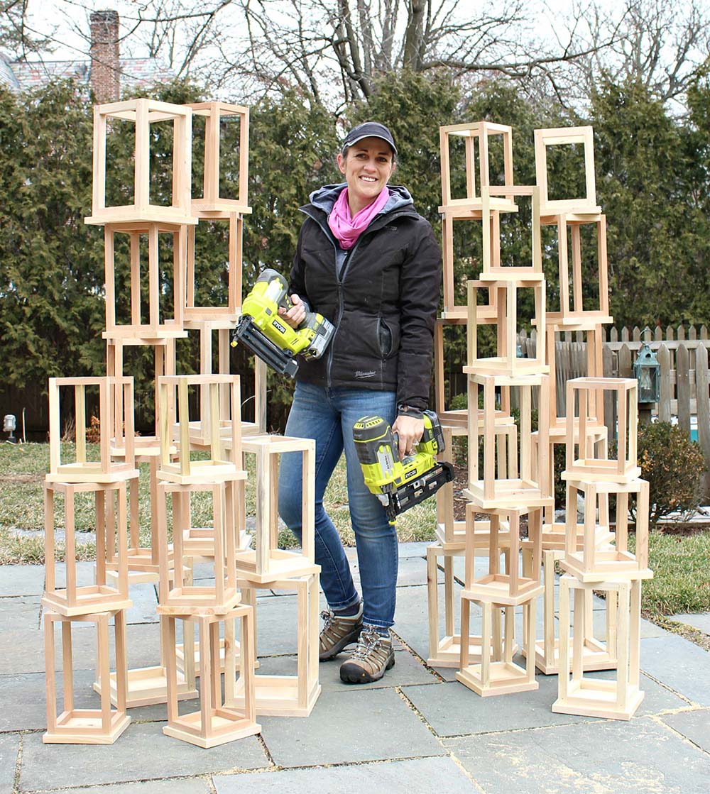 A woman standing between two towers of DIY Wooden Lanterns.