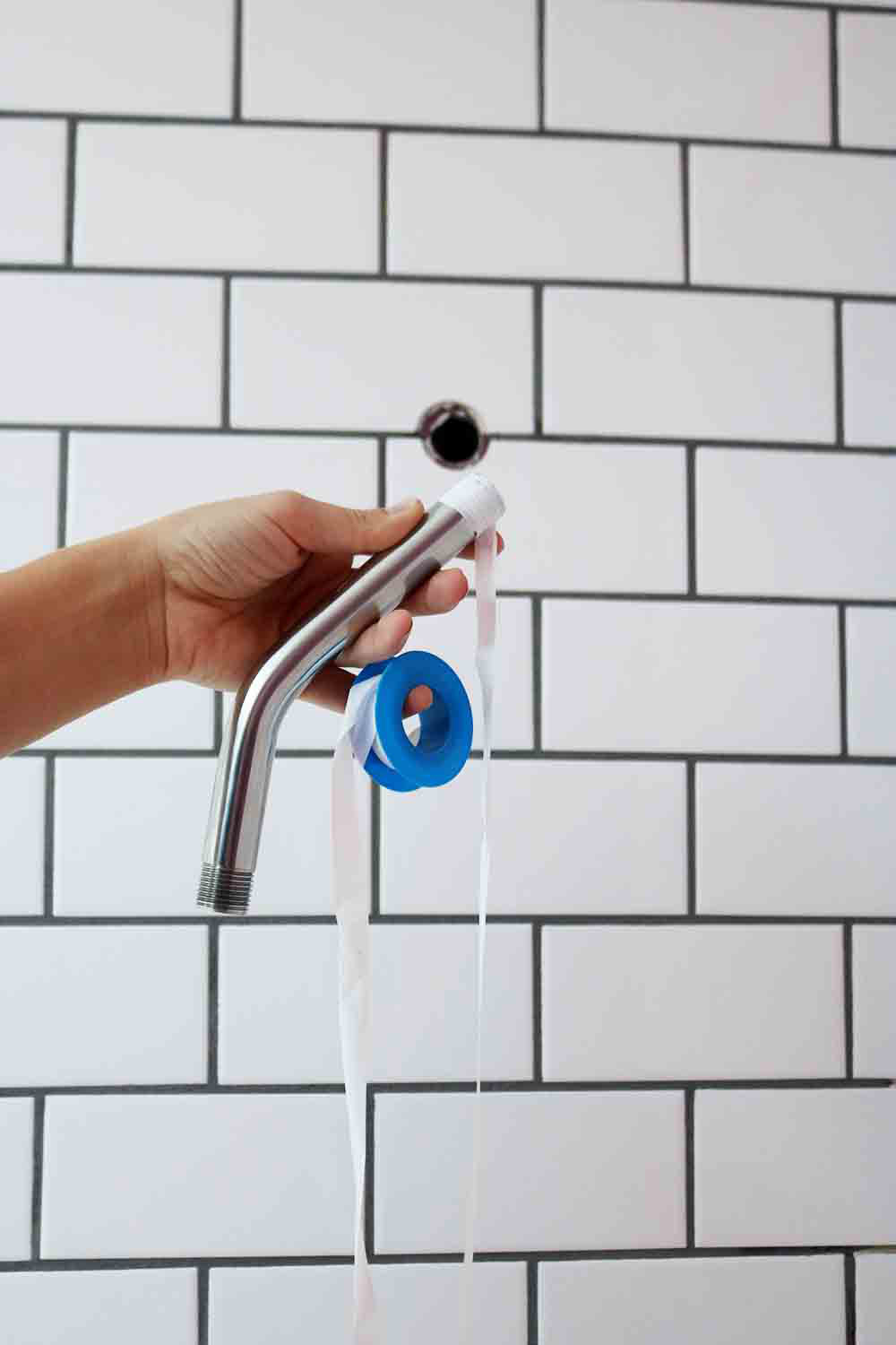 A person removing an old shower head from a tile wall.