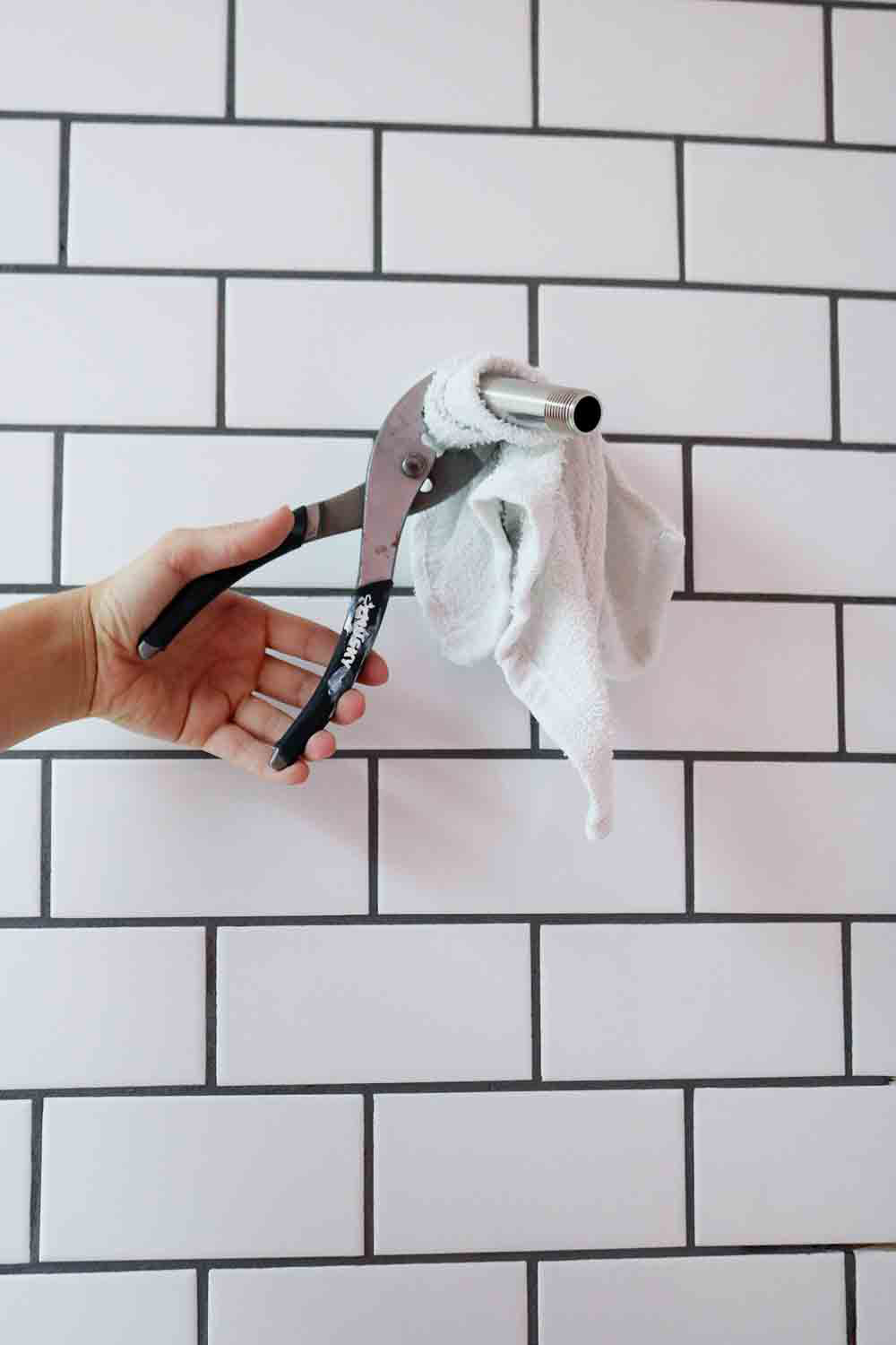 A person using pliers to remove an old shower head from a tile wall.