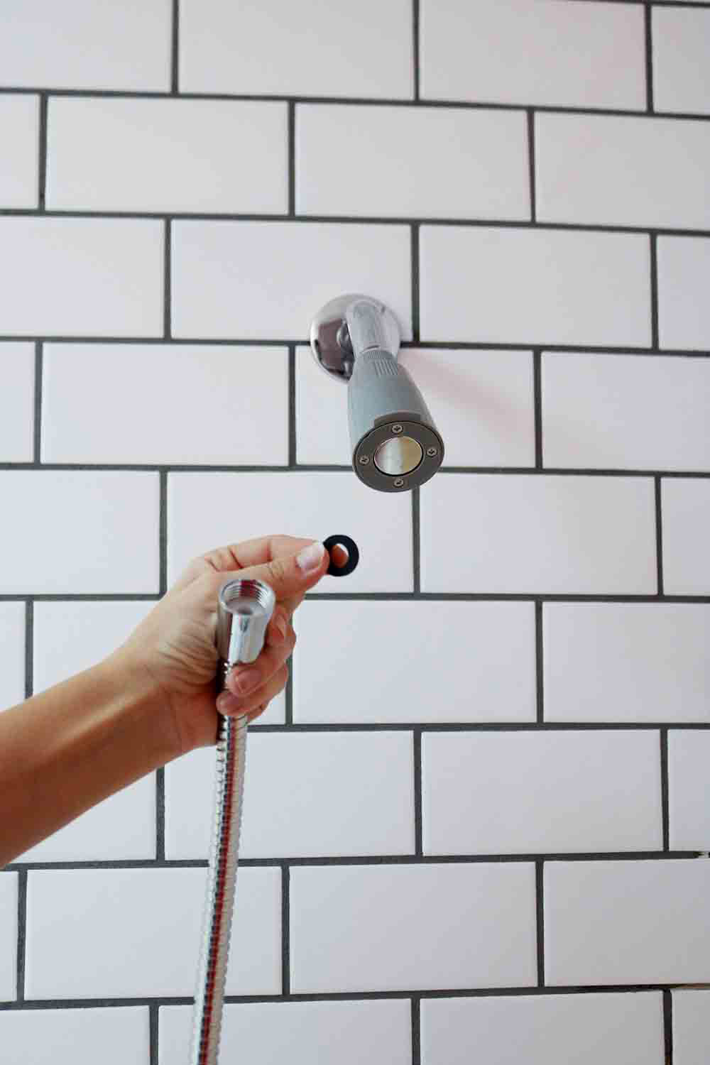 A person attaching a new shower head base onto a wall.