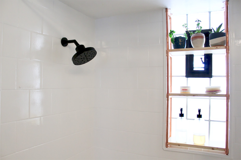 A shower with white painted tile and a black showerhead.