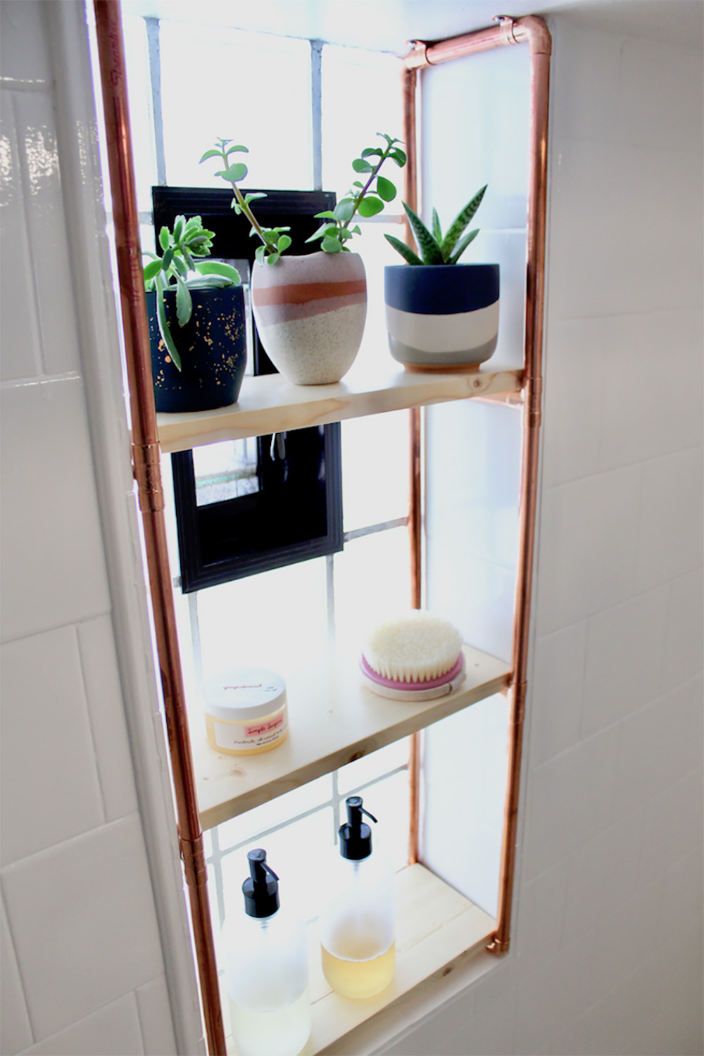 A shower window opening with a three-tier shelf built from copper pipes and pine boards.