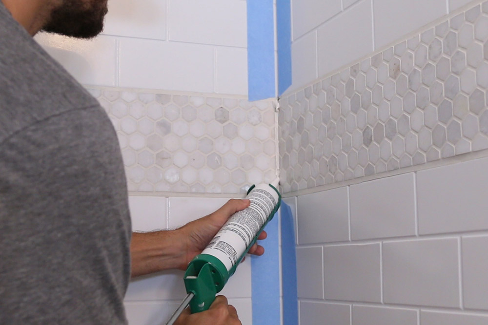 A person caulking shower tiles. A person caulking shower tiles.