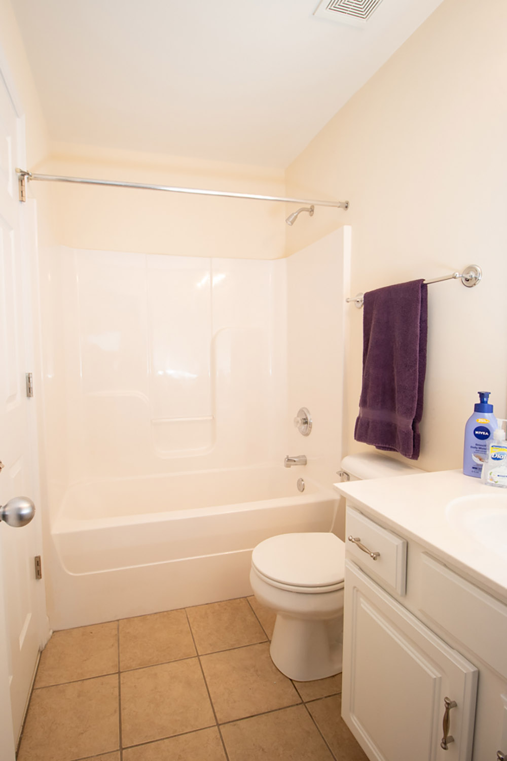 A bathroom with ivory walls, white shower tile, white vanity, brown tile floor and a purple towel. A bathroom with ivory walls, white shower tile, white vanity, brown tile floor and a purple towel.