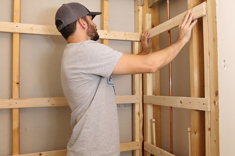 A person installing wooden framing for shower walls. A person installing wooden framing for shower walls.