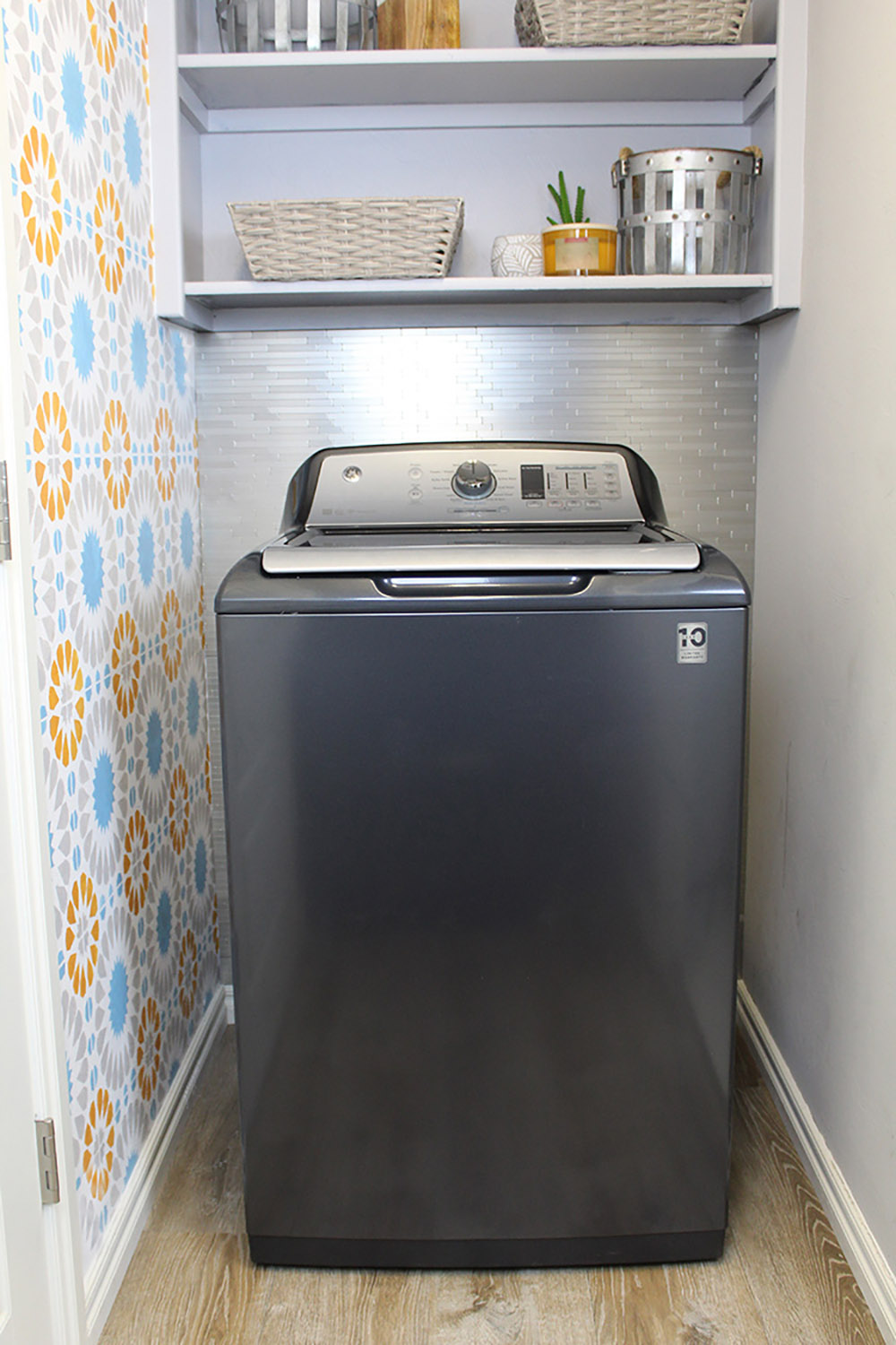 A gray GE washing machine in front of a wall of metal backsplash.