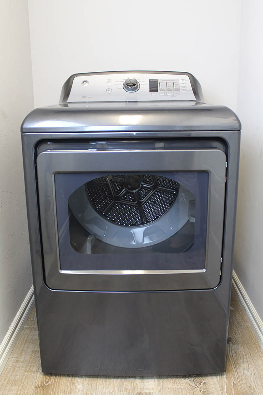 A gray GE dryer sits in an empty laundry room with blank walls.
