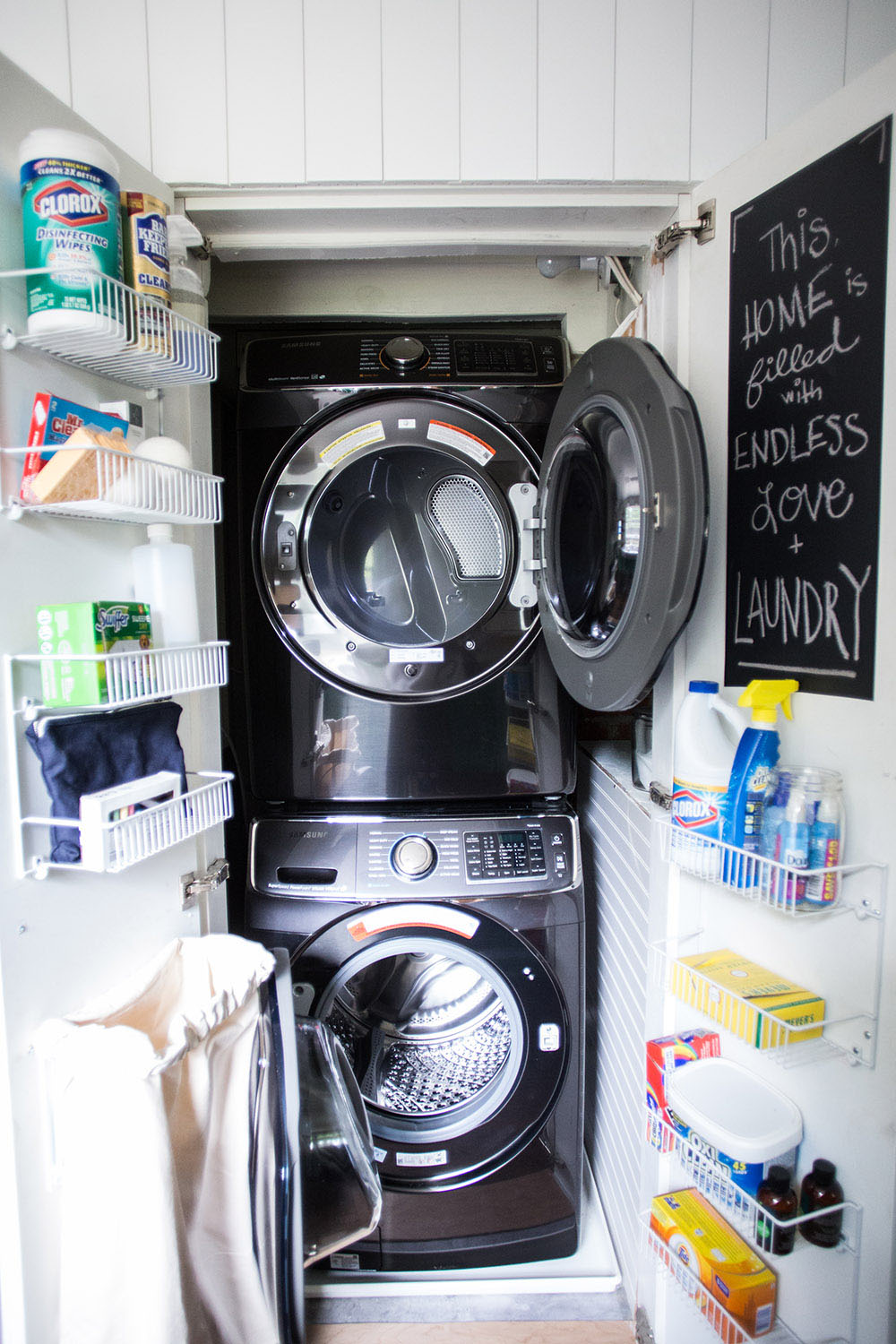 A closet with a open washing machine, a dryer, and shelves on the doors.