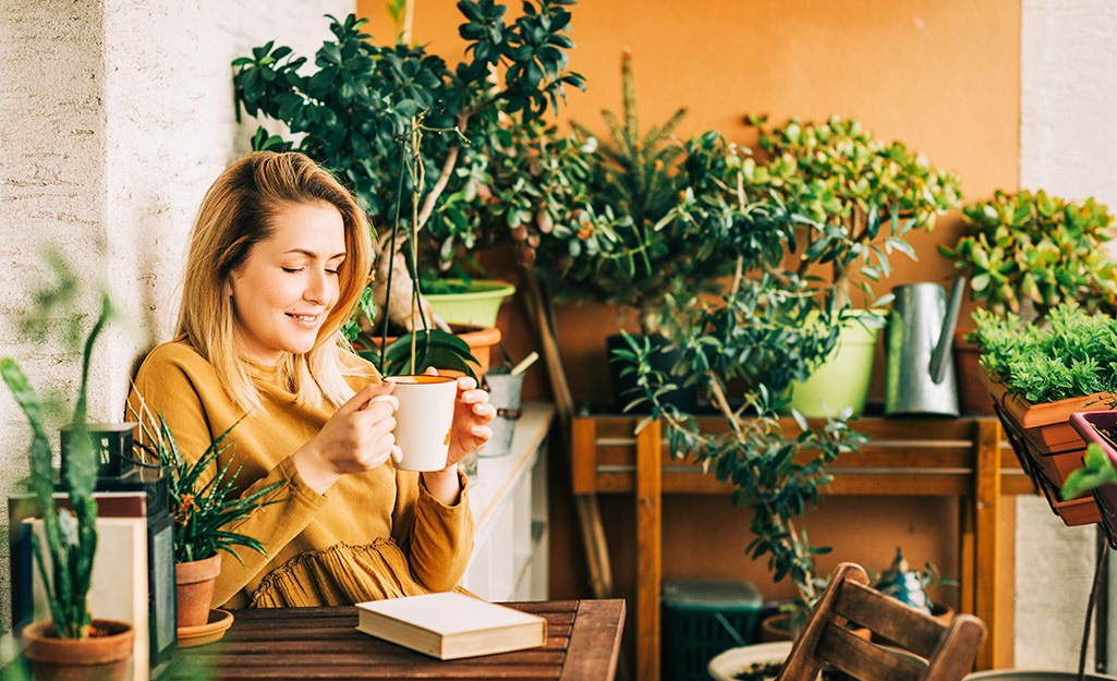 A person sitting at a patio table next to a wall with potted plants.