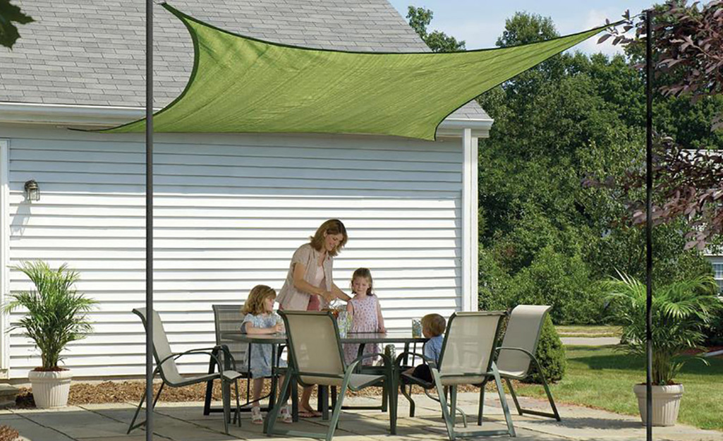 A family gathered around a patio dining set covered by a sun sail