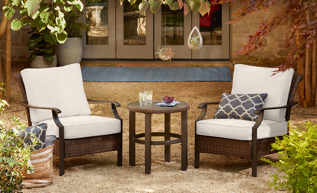 Two chairs and a side table surrounded by plants on a small patio.