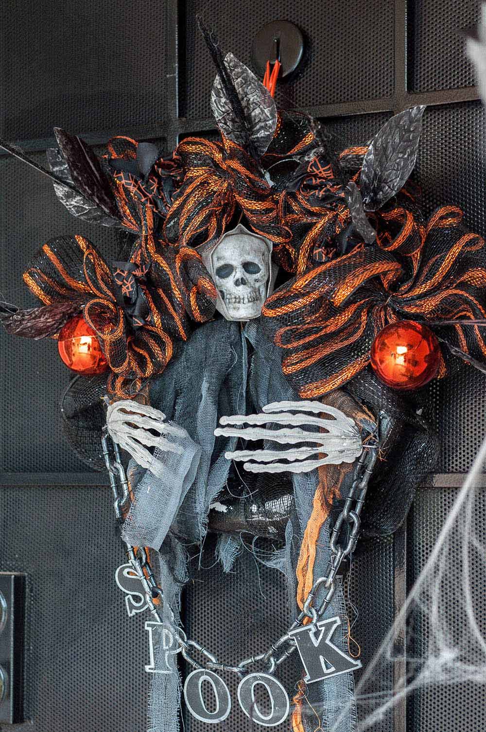An orange and black Halloween wreath with a skeleton and chains decorates a front door.