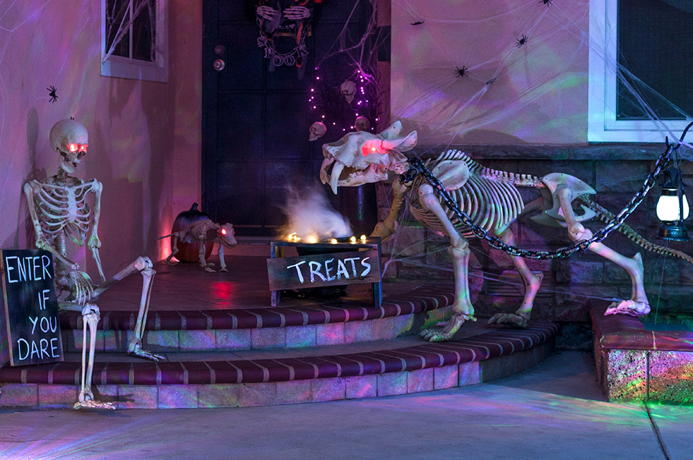 A small porch decorated for Halloween with skeletons and purple lights.