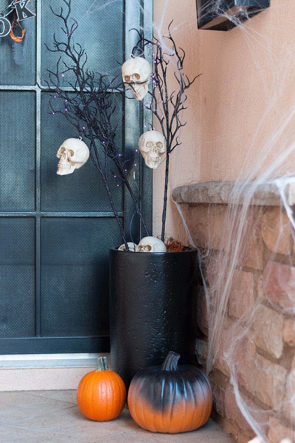 A tall black planter with faux branches, skull heads, and purple lights.