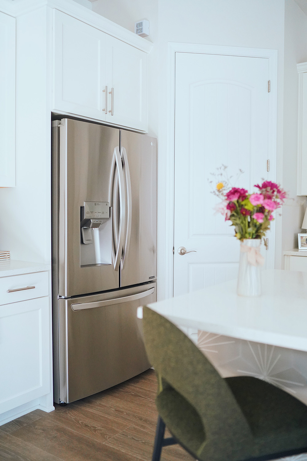 A white kitchen with a new stainless steel LG refrigerator.