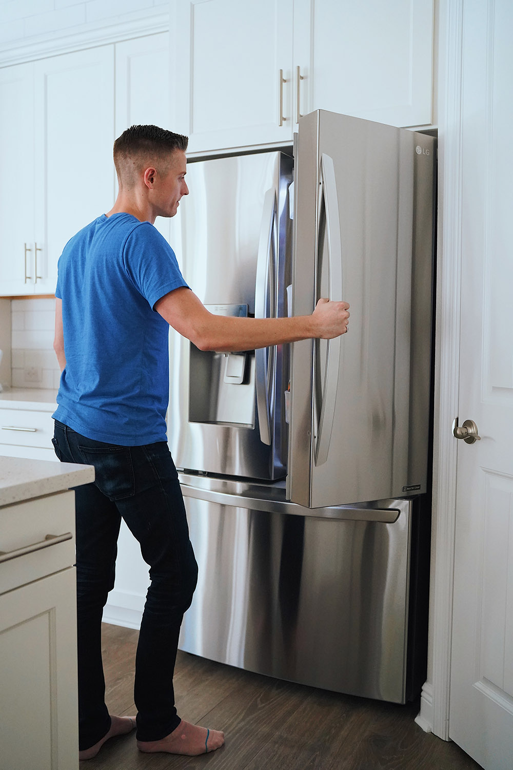 A man standing in front of a refrigerator holding the door open.