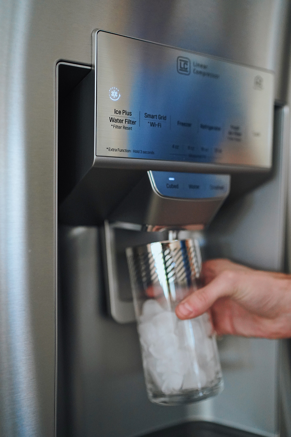 A person using an LG refrigerator to fill up a glass of water.