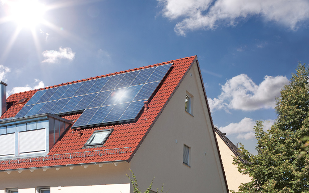 The sun shines brightly on solar panels atop a roof. 