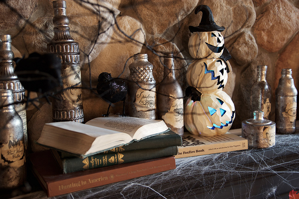 A mantel decorated with stacked pumpkins, books, and DIY potion bottles.