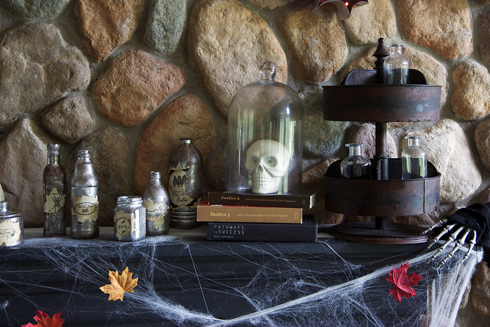 A skull sitting under a glass jar surrounded by spider webs decorates a mantel for Halloween.