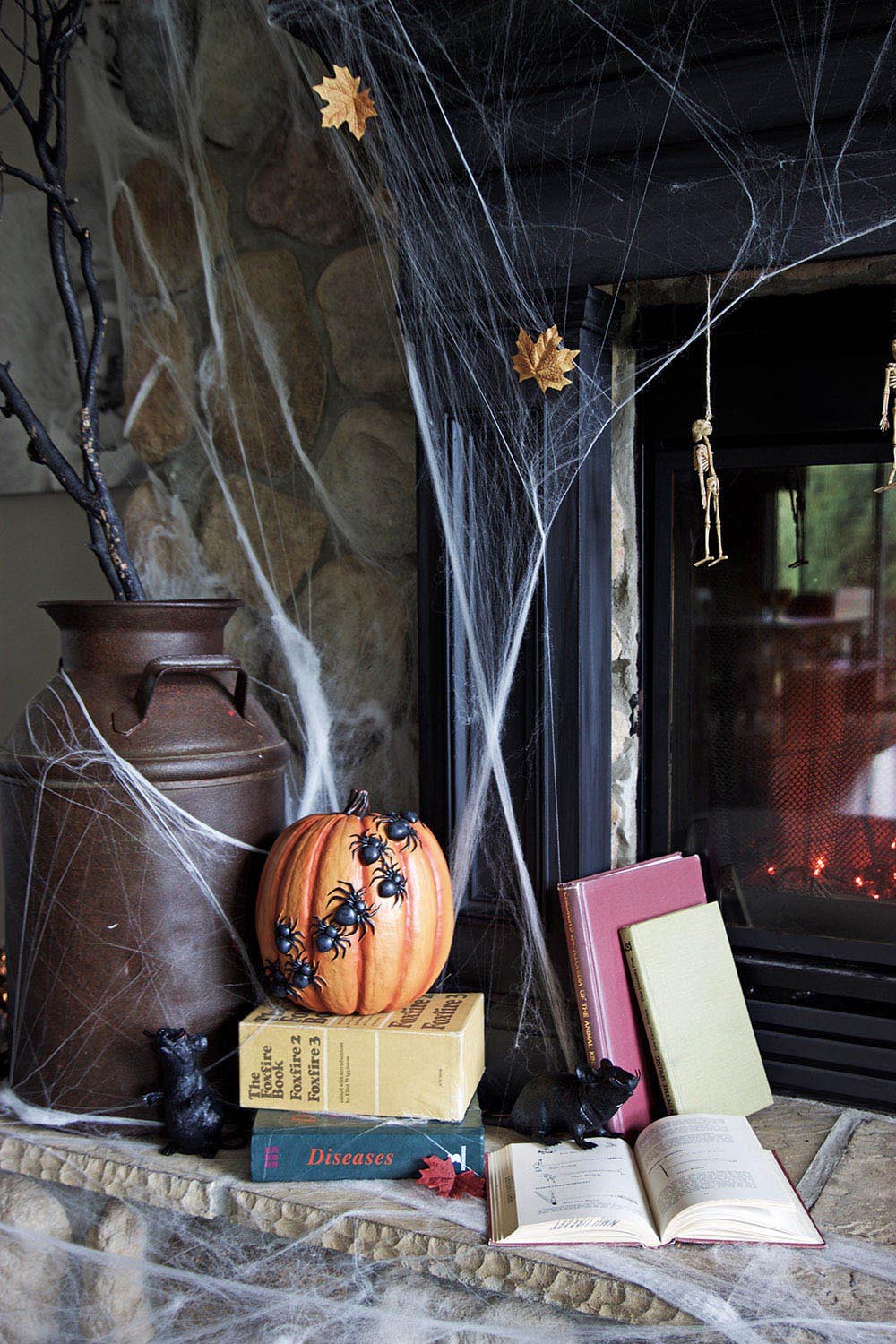 A milk jug filled with dead tree branches sits on a fireplace next to a pumpkin with spiders on it.