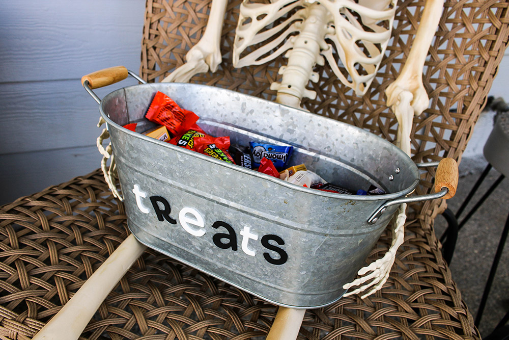 A tin of treats is held by a skeleton sitting in a chair.