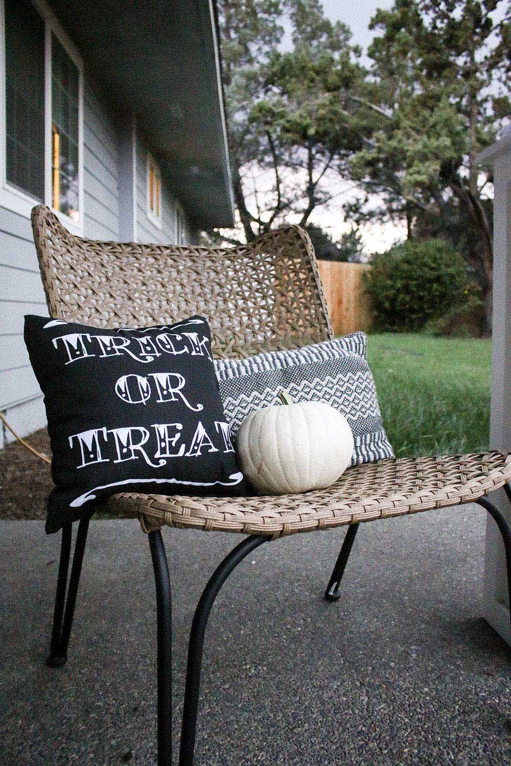 A chair decorated with pillows and a white pumpkin.