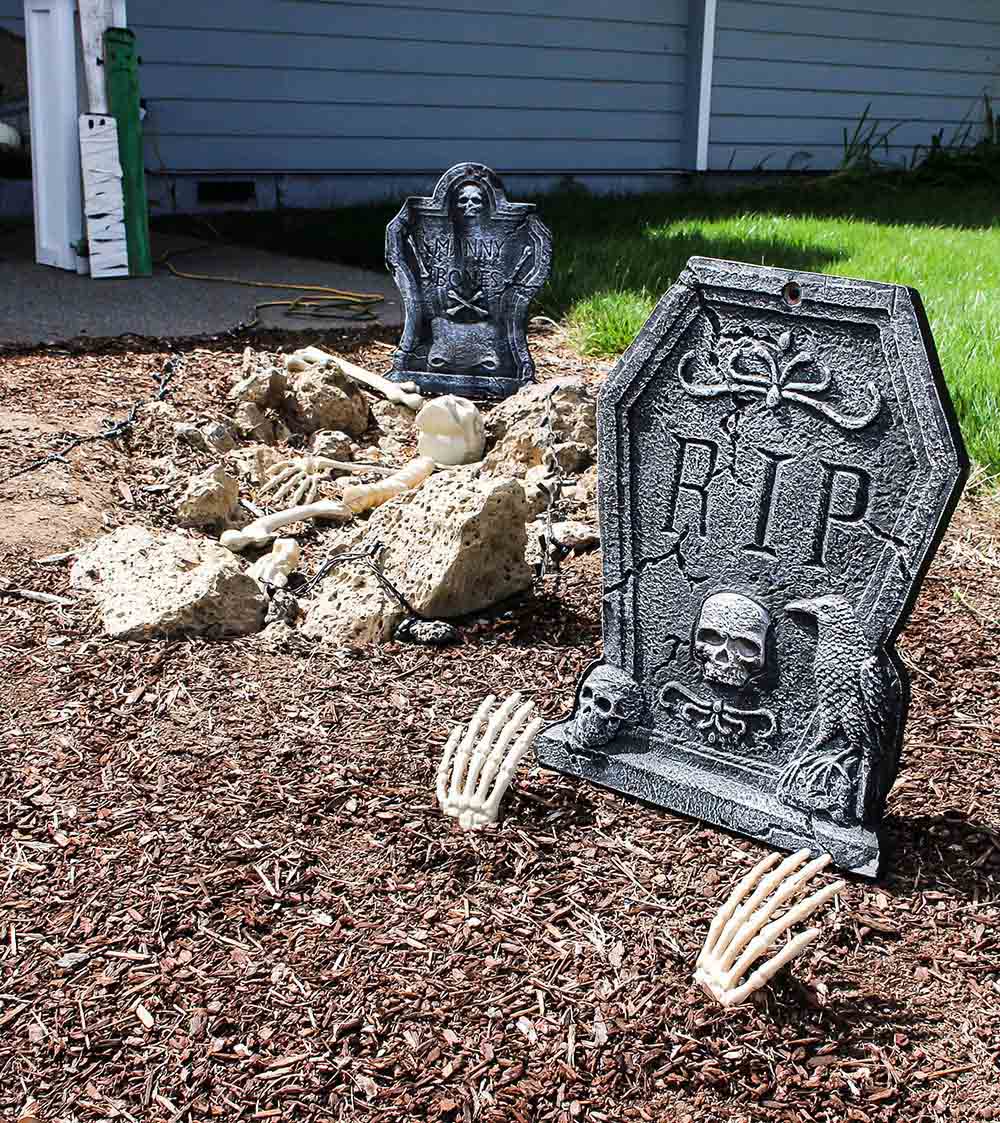 A spooky Halloween cemetery with tombstones, bones, and skeleton hands sticking out of the ground.