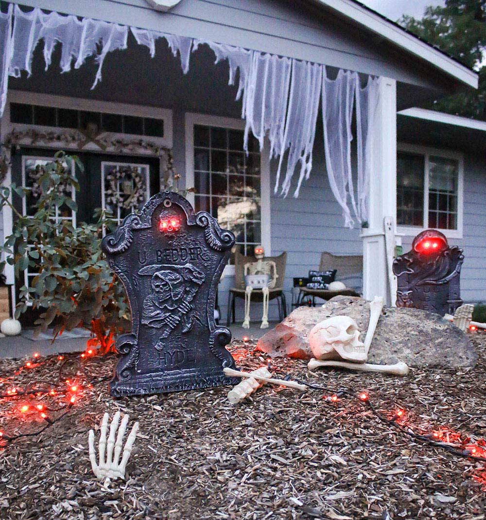 A front yard decorated with orange lights and tombstones with glowing eyes.