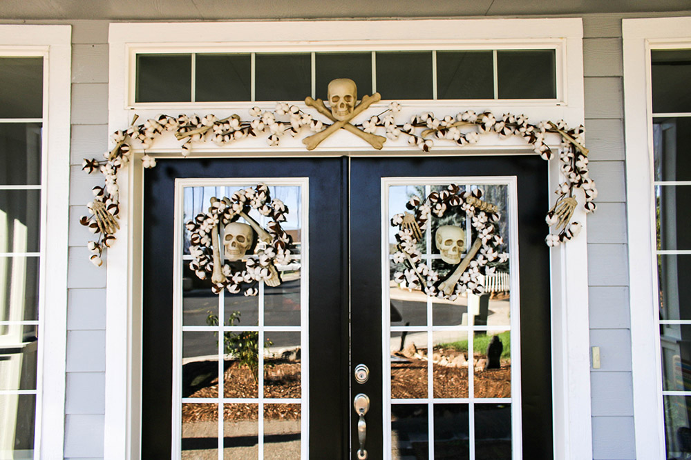 A cotton garland with a skull and crossbones hangs over double doors decorated with skull wreaths.