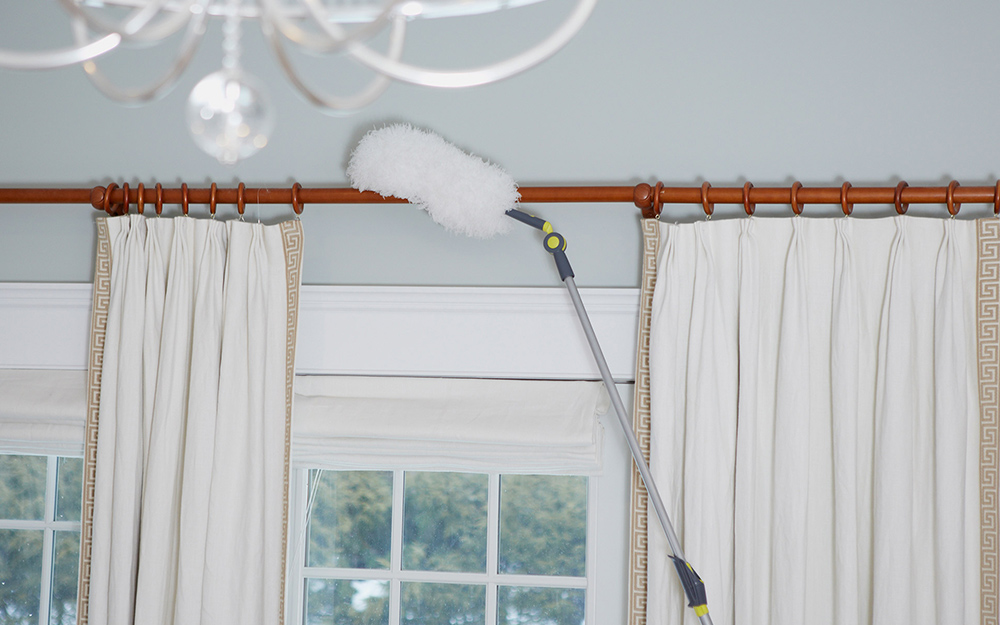 A long-handled duster being used to clean a curtain rod