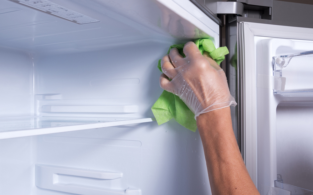 A person using a cloth to wipe the interior of a refrigerator