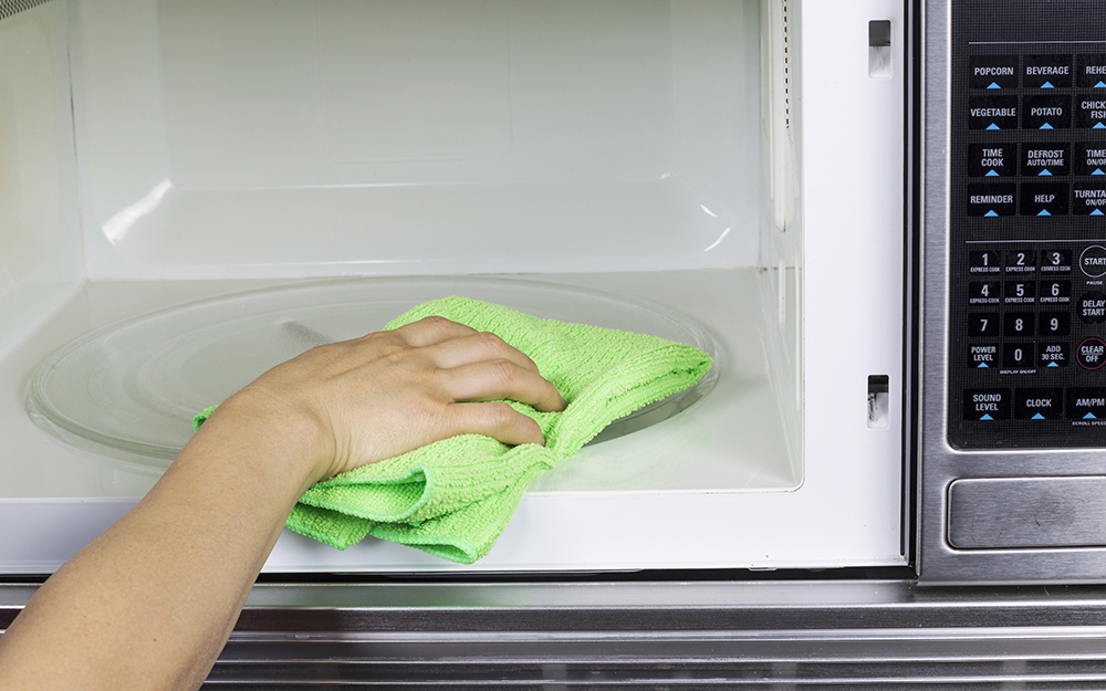 A person using a cloth to clean the interior of a microwave