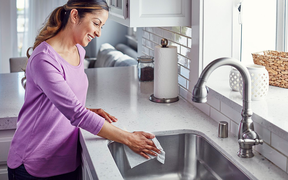 Woman cleaning a kitchen sink with a cloth