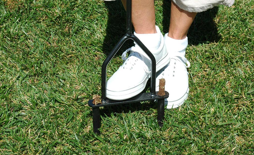 A person uses an aerator to aerate the soil in a yard.