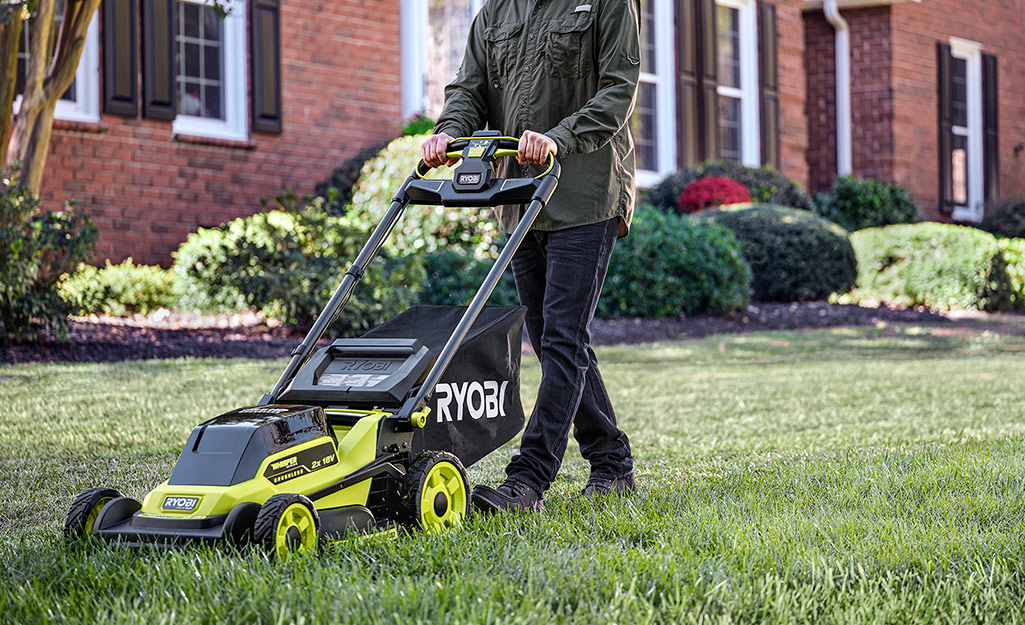 A person mows a lawn with a lawnmower.