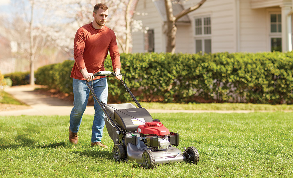A person mows a lawn with a lawnmower.