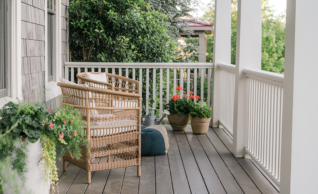 A wicker chair and pots of flowers on a porch.