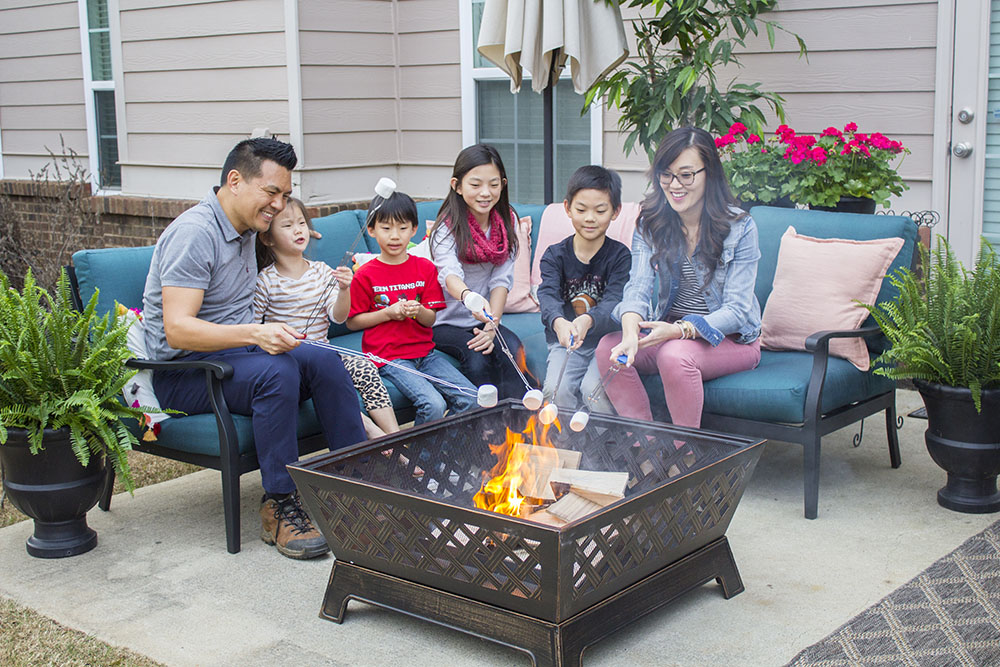 A family sits on an outdoor sectional while roasting marshmallows over a fire pit. A family sits on an outdoor sectional while roasting marshmallows over a fire pit.