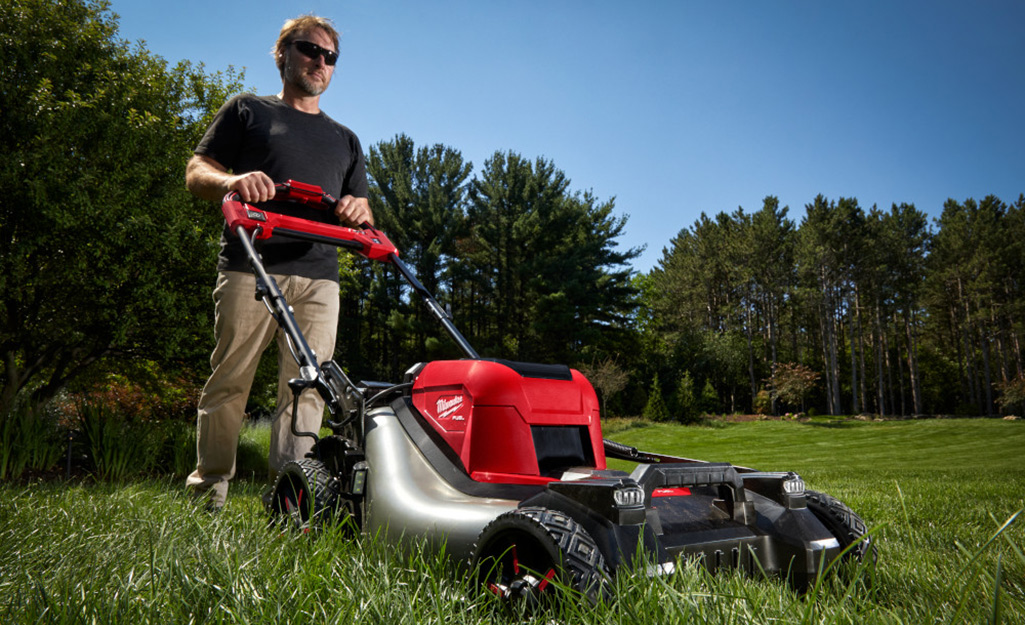 A person mowing their lawn with a lawn mower to prep it for a square foot garden.