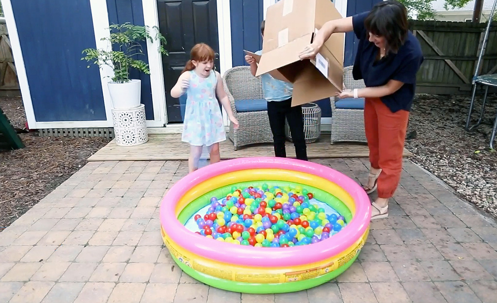 A woman pouring balls into an inflatable pool.