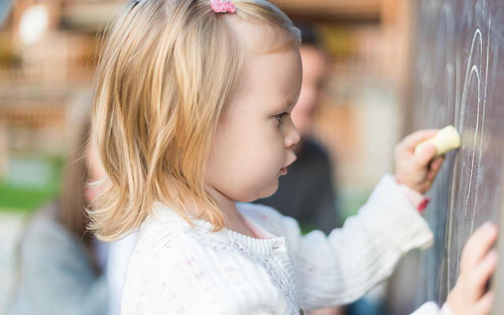 A little girl draws on an outdoor chalkboard. A little girl draws on an outdoor chalkboard.