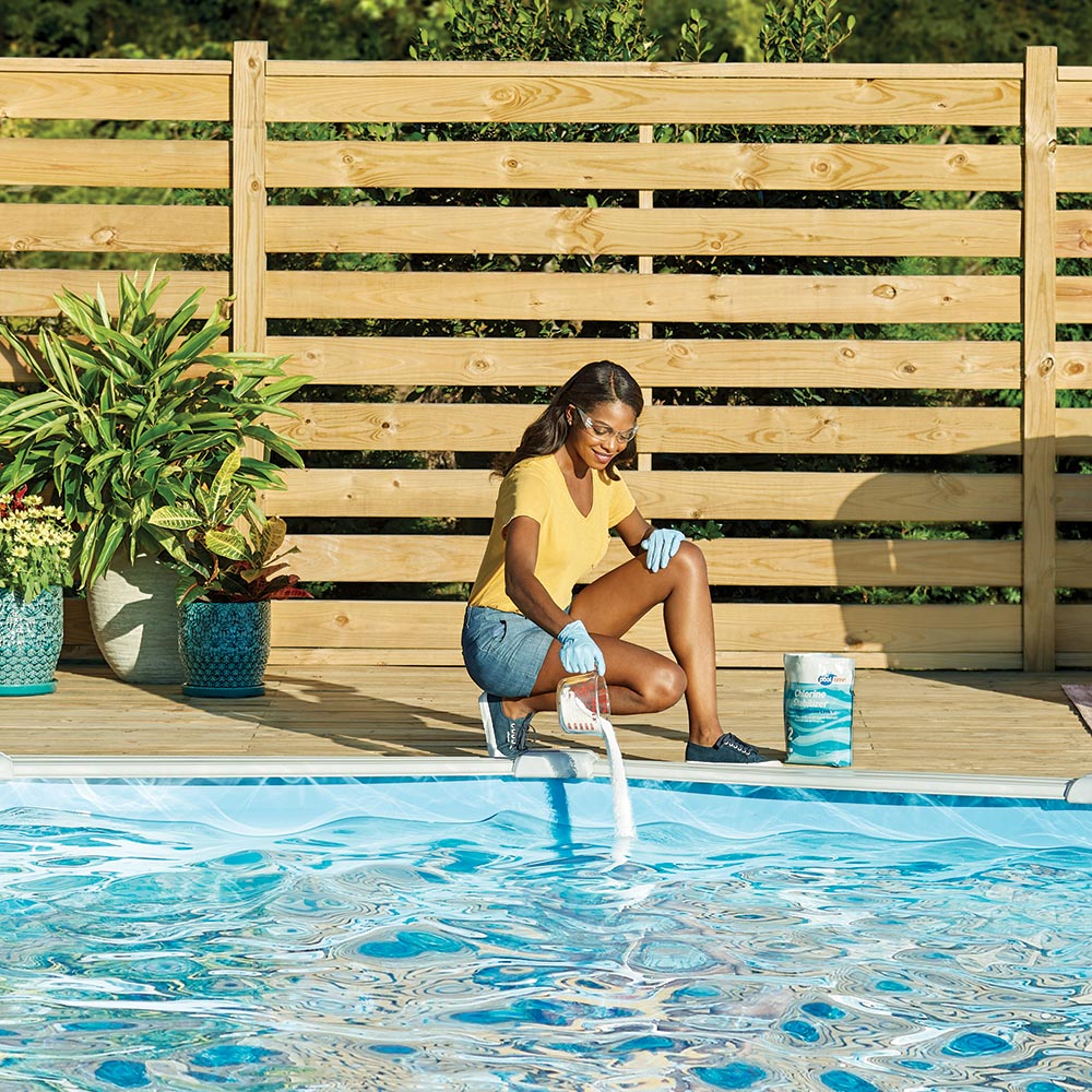 A woman wearing safety glasses and gloves adds pool shock to her swimming pool.