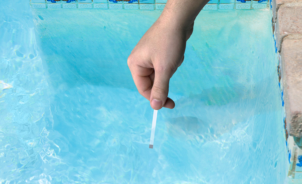 A person dips a pool testing strip into a swimming pool.