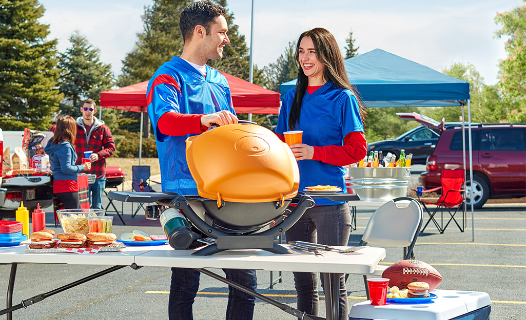 Two people use a portable grill at a tailgate. 