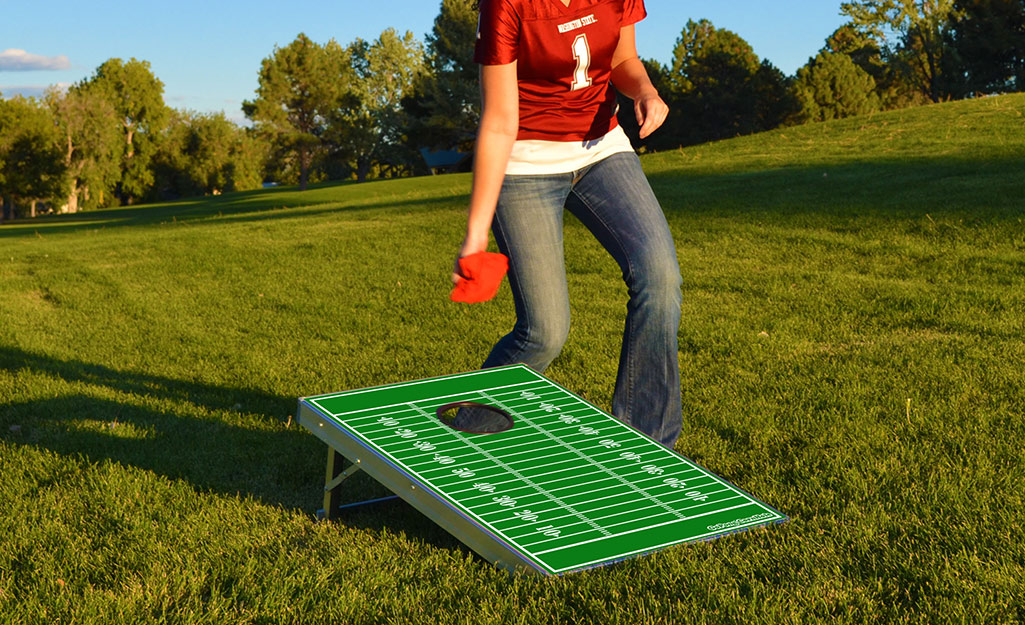 A woman plays a game of cornhole on the lawn during a tailgate. 