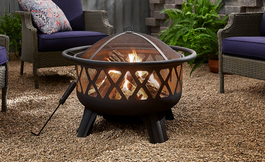 A fire pit sits in the middle of lawn furniture in a backyard.