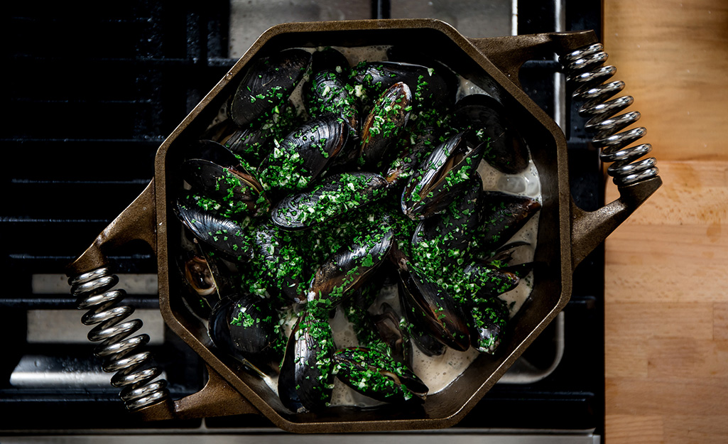 Mussels in a black Dutch oven on a stove top.