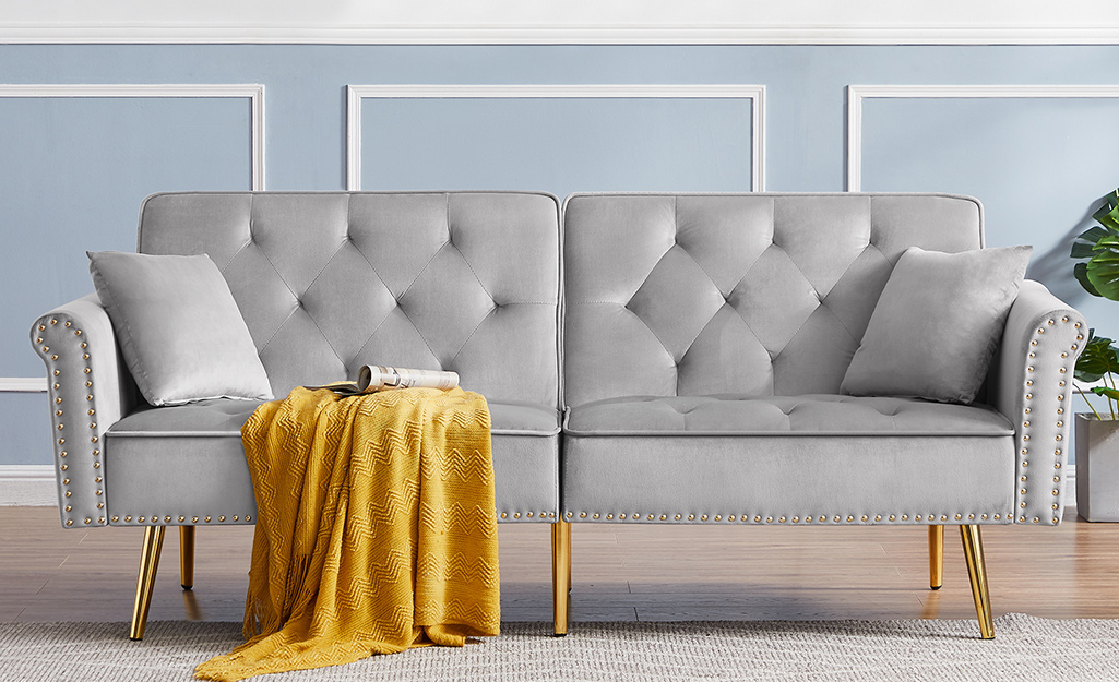 A grey tufted loveseat futon in front of a blue wall.