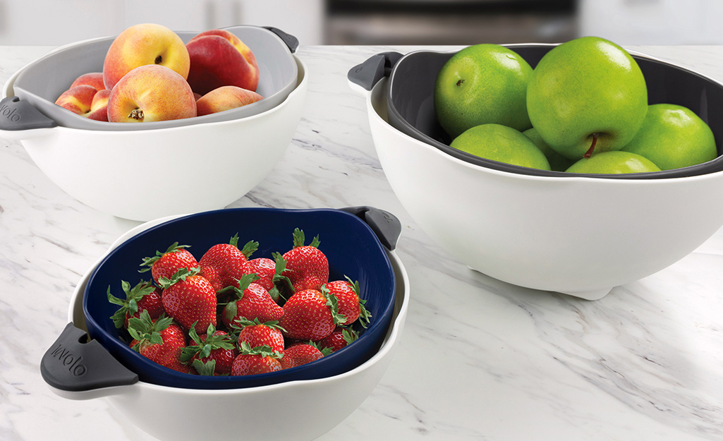 One mixing bowl with handles holds green apples, another holds strawberries and a third holds red apples. 